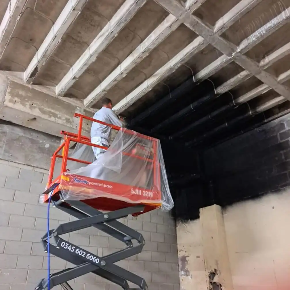 Commercial decorator on a scissor lift painting a high industrial ceiling – Fineline Decorators Plymouth